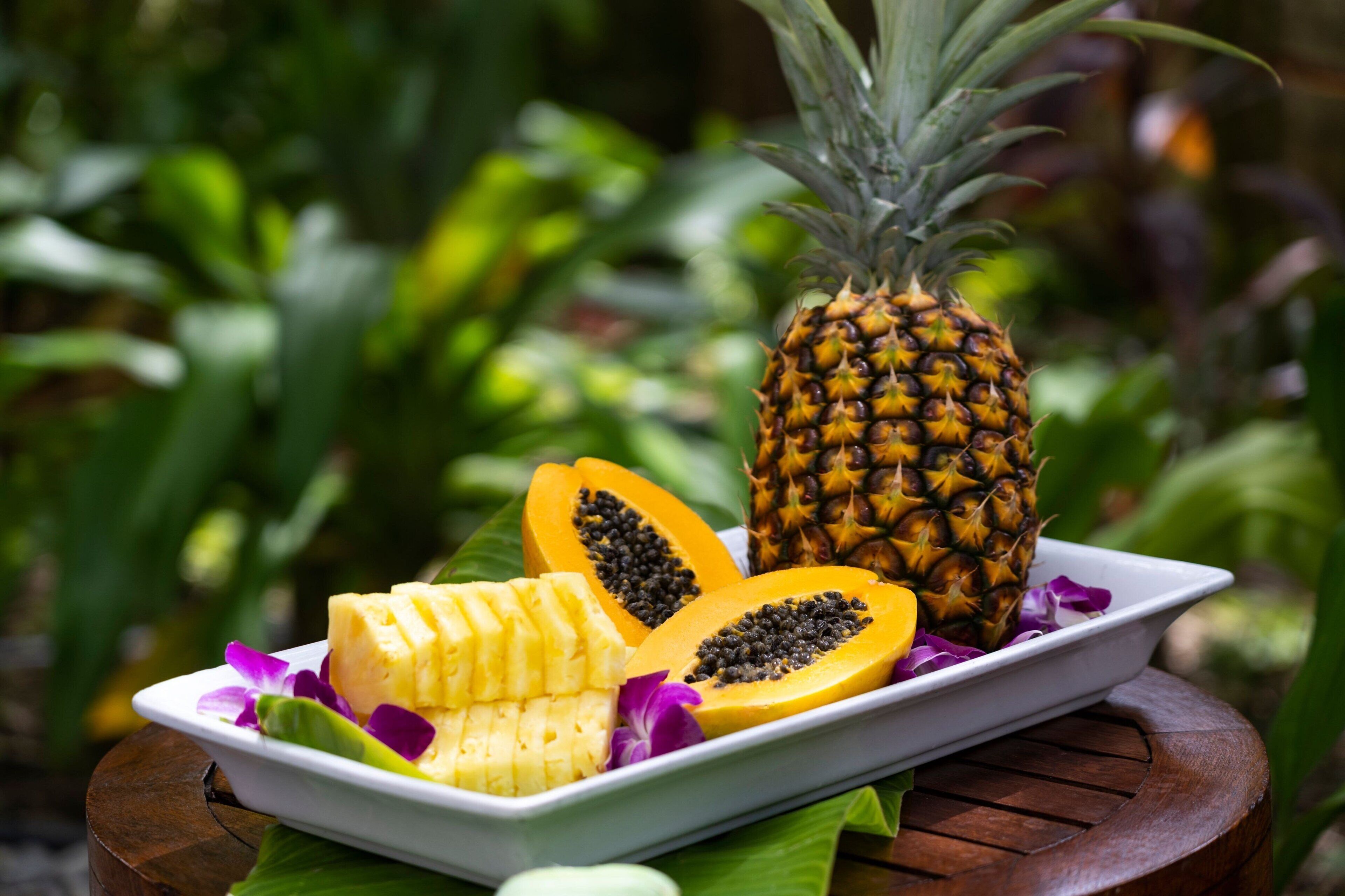 Une assiette contenant des tranches d’ananas, de papaye et de banane, posée sur une table en bois.