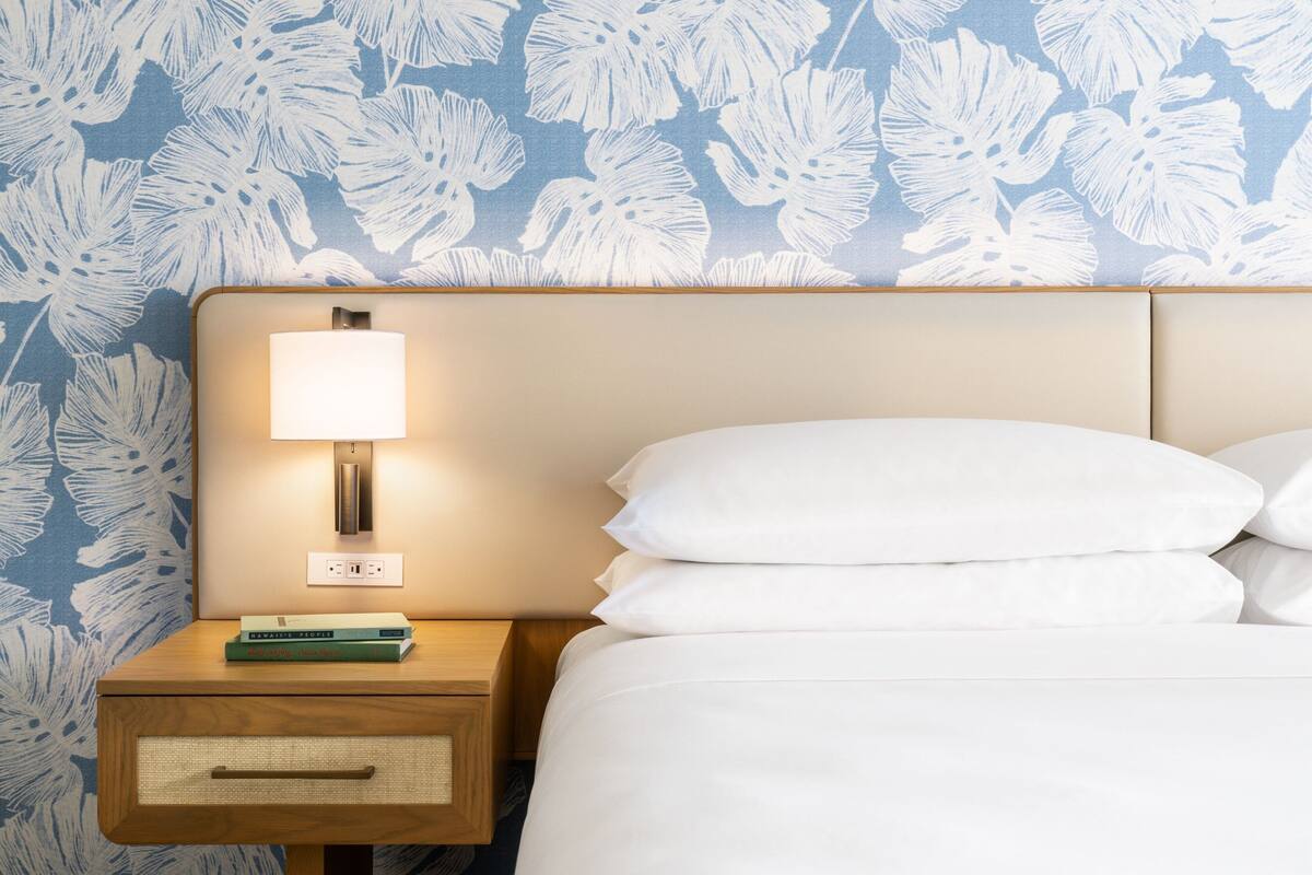 A neatly made bed with white pillows and a headboard with a wall-mounted lamp.