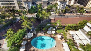 Un resort con piscina central rodeada de palmeras y tumbonas, con vista a una playa y al océano.