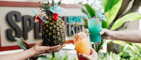 A person holding a pineapple with a drink in another hand.