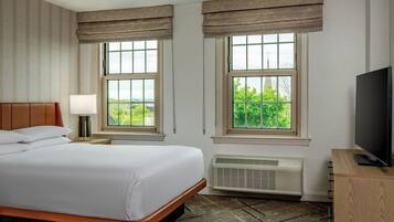 Una habitación de hotel con una cama, dos ventanas con cortinas, un televisor sobre un soporte de madera y un calentador.