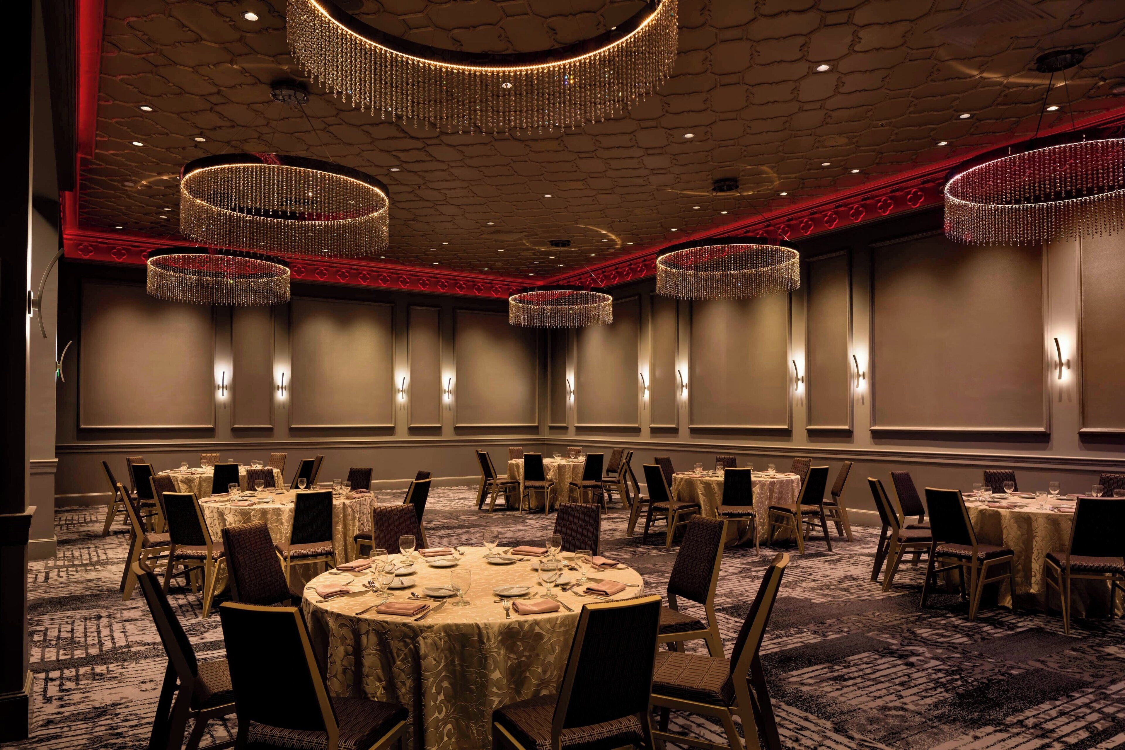 A banquet hall with round tables, chairs, and chandeliers.