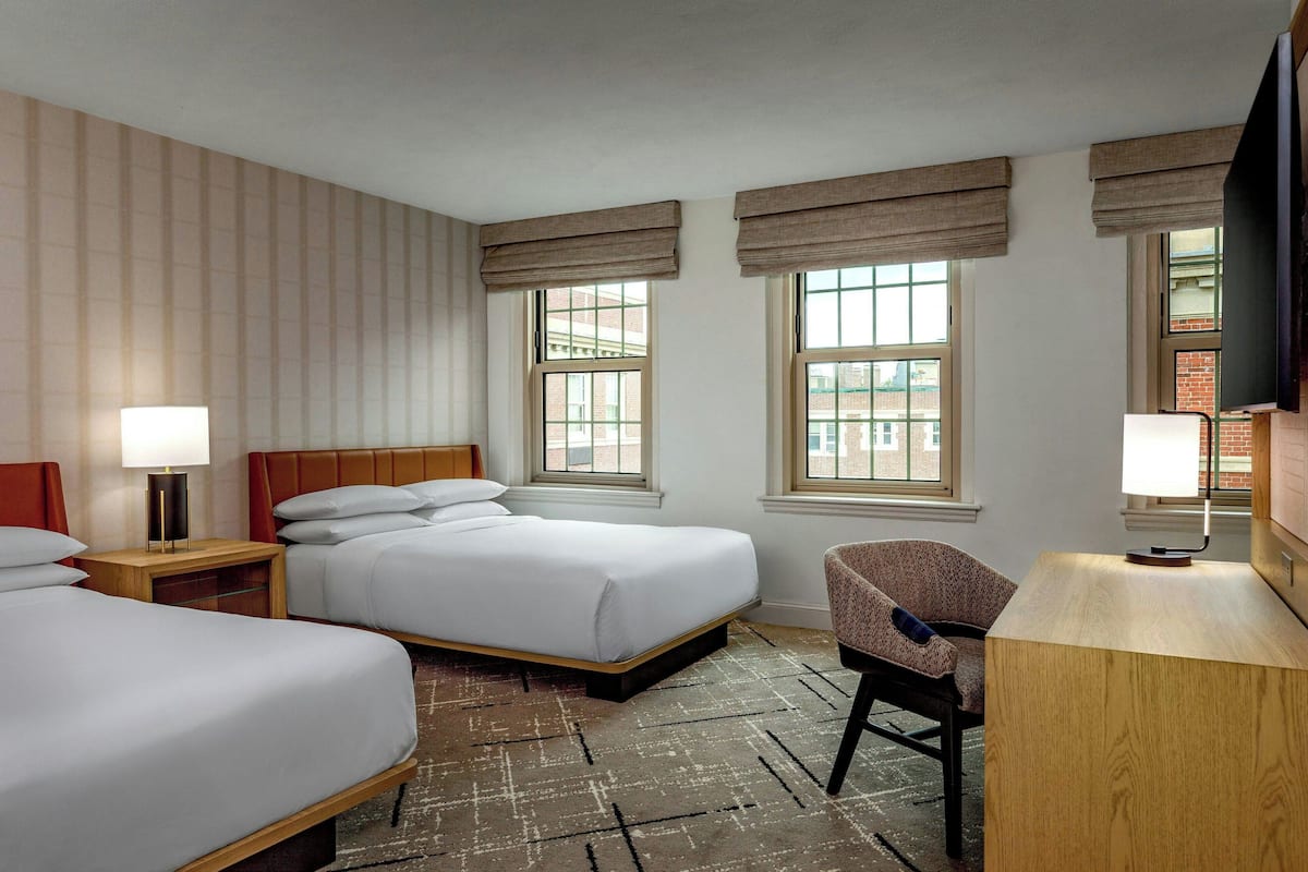 A hotel room with two beds, a desk, a chair, and a TV.