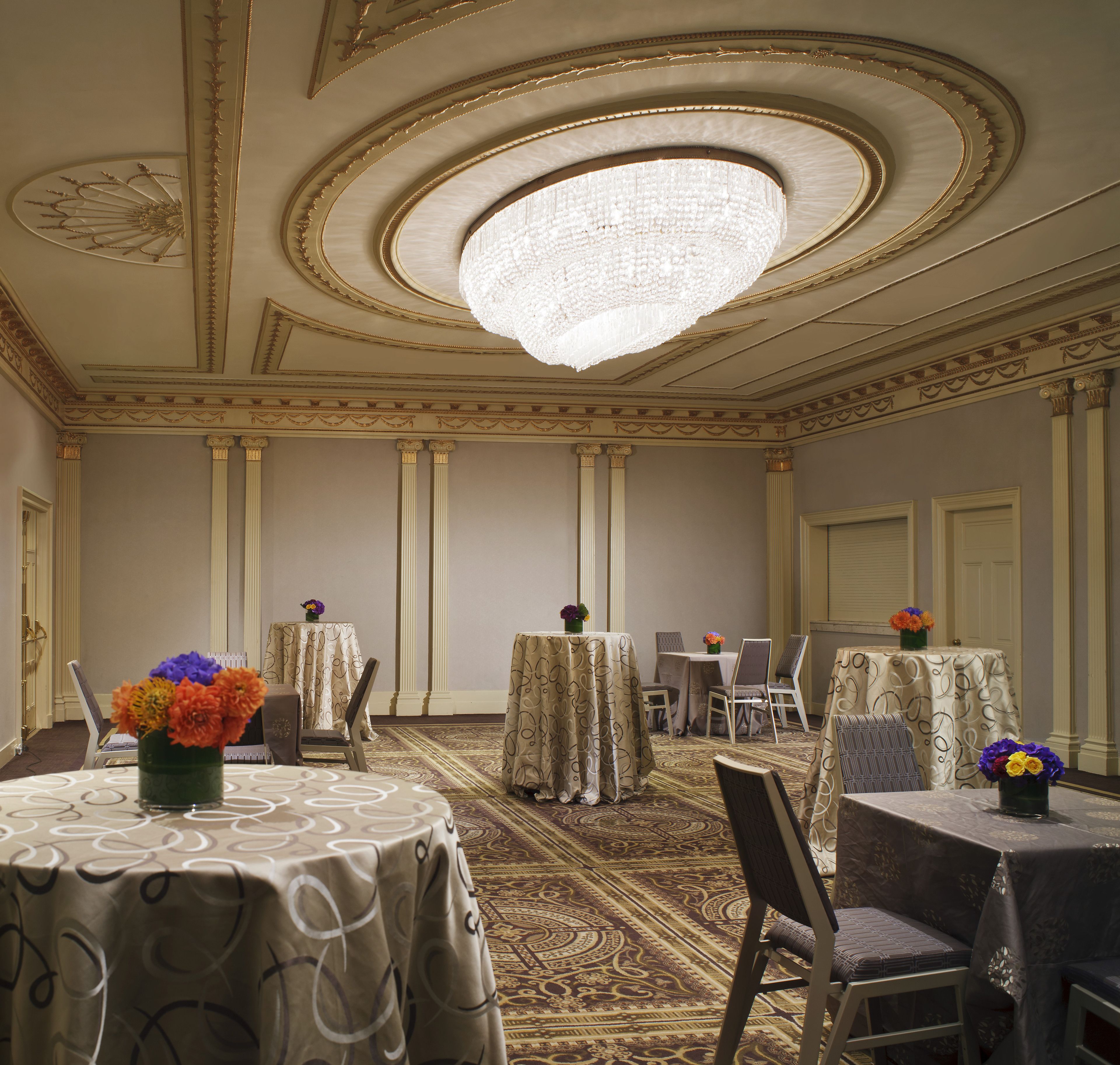 A hotel room with a chandelier, round tables, and chairs.