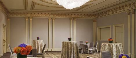 A hotel room with a chandelier, round tables, and chairs.