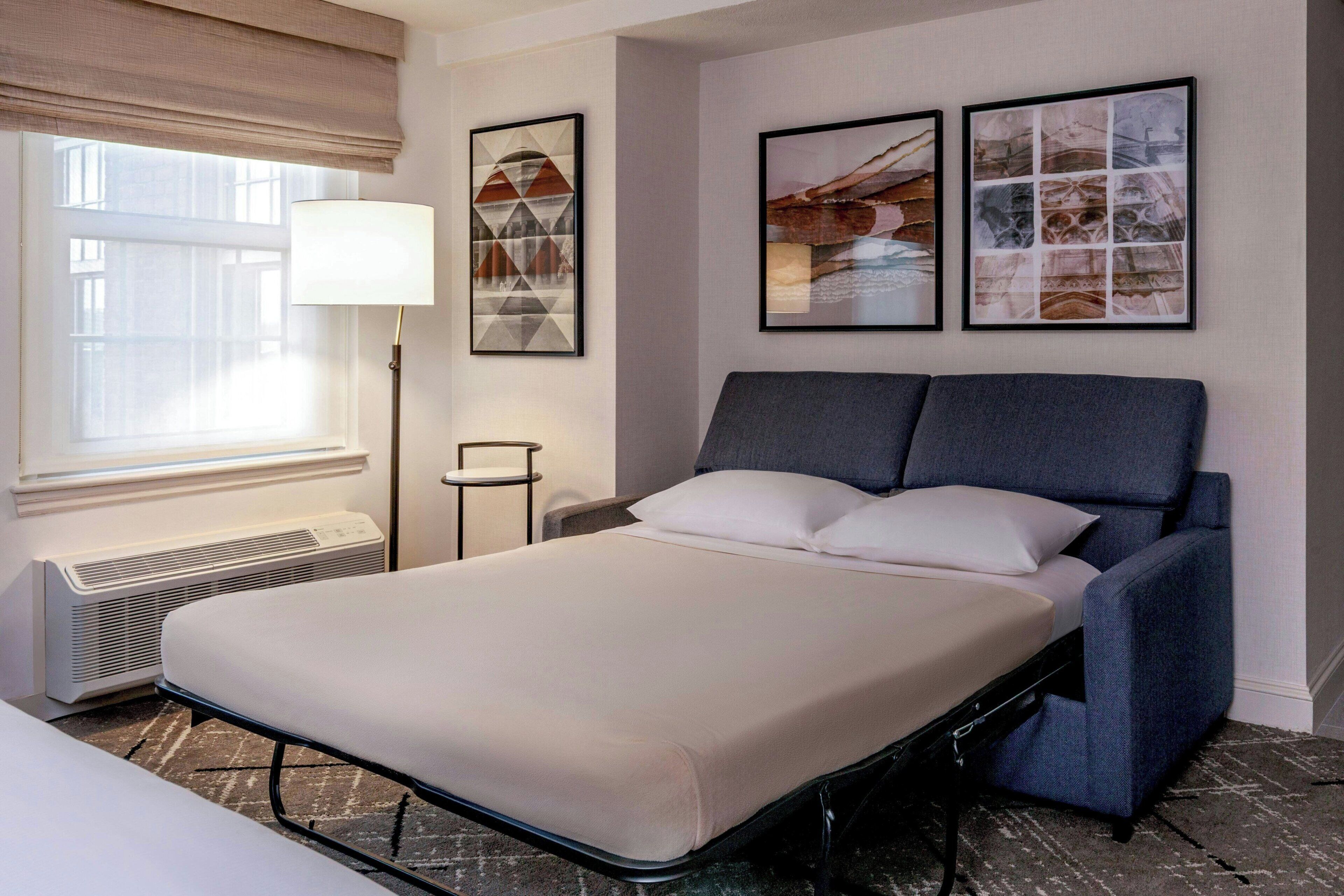 Una habitación de hotel con una cama, una lámpara de pie y dos cuadros en la pared.