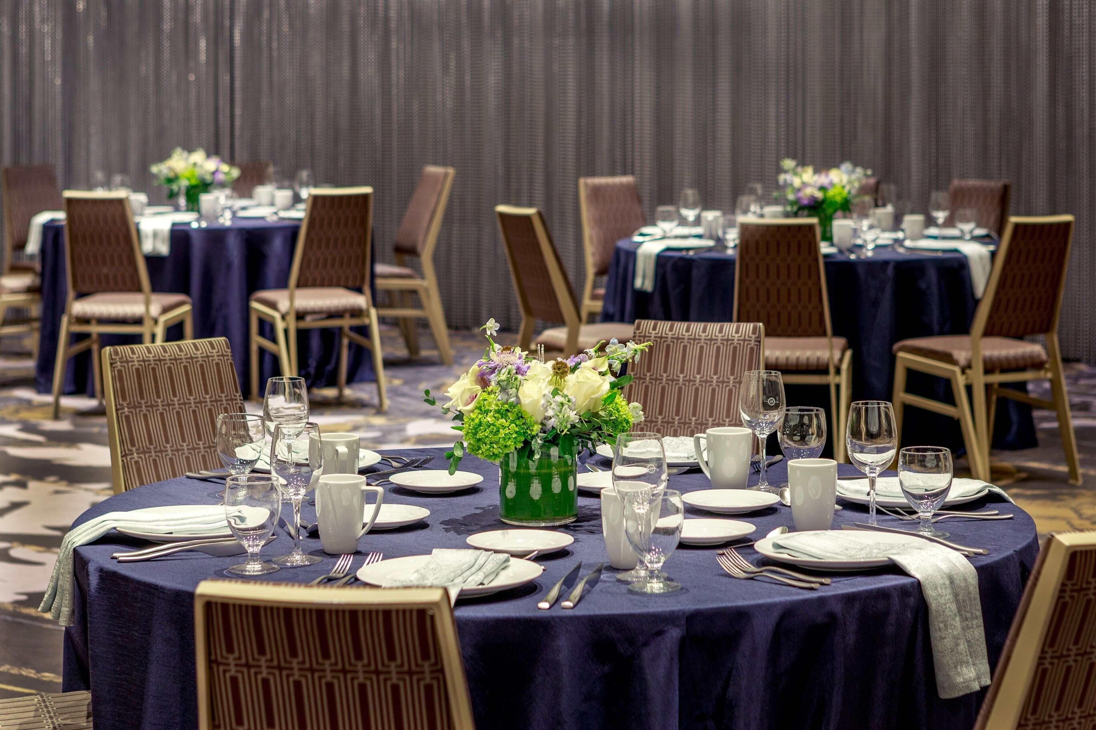 A banquet hall with round tables set for dining, each with chairs, plates, cutlery, and glassware.