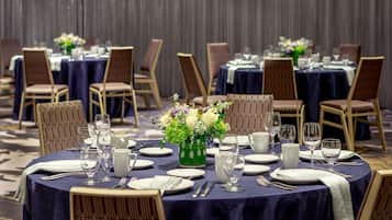 A banquet hall with round tables set for dining, each with chairs, plates, cutlery, and glassware.