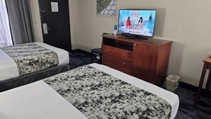 Ein Hotelzimmer mit zwei Betten, einem Fernseher, einer Holzkombination und einer Tür.