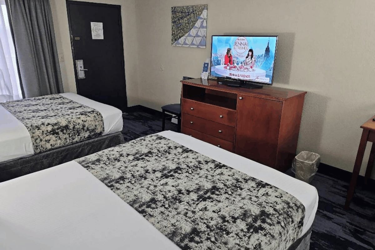 A hotel room with two beds, a TV, a wooden dresser, and a door.