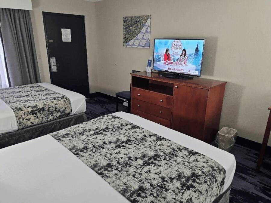 Habitación de hotel con dos camas, un televisor, un aparador de madera y una puerta.