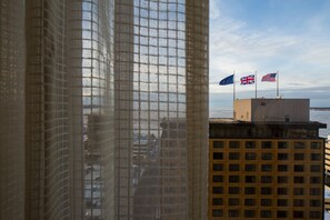 A view through a window with a mesh screen, featuring a building with multiple flags, including the UK and US flags, and a body of water in the background. - Hotel Captain Cook (Anchorage)