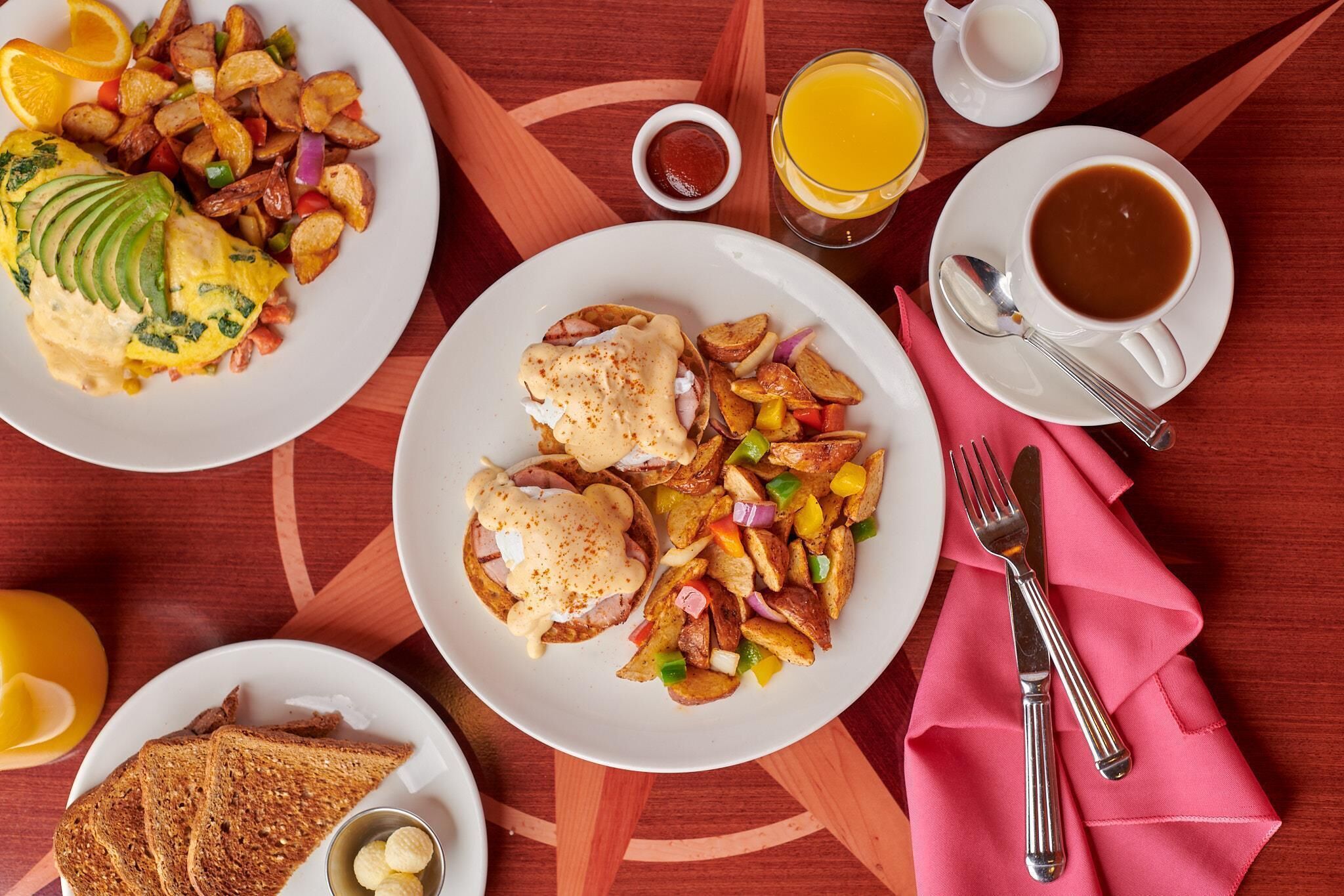 A breakfast setting with plates of food, a glass of orange juice, a cup of coffee, and a napkin with cutlery.