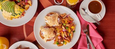 A breakfast setting with plates of food, a glass of orange juice, a cup of coffee, and a napkin with cutlery.