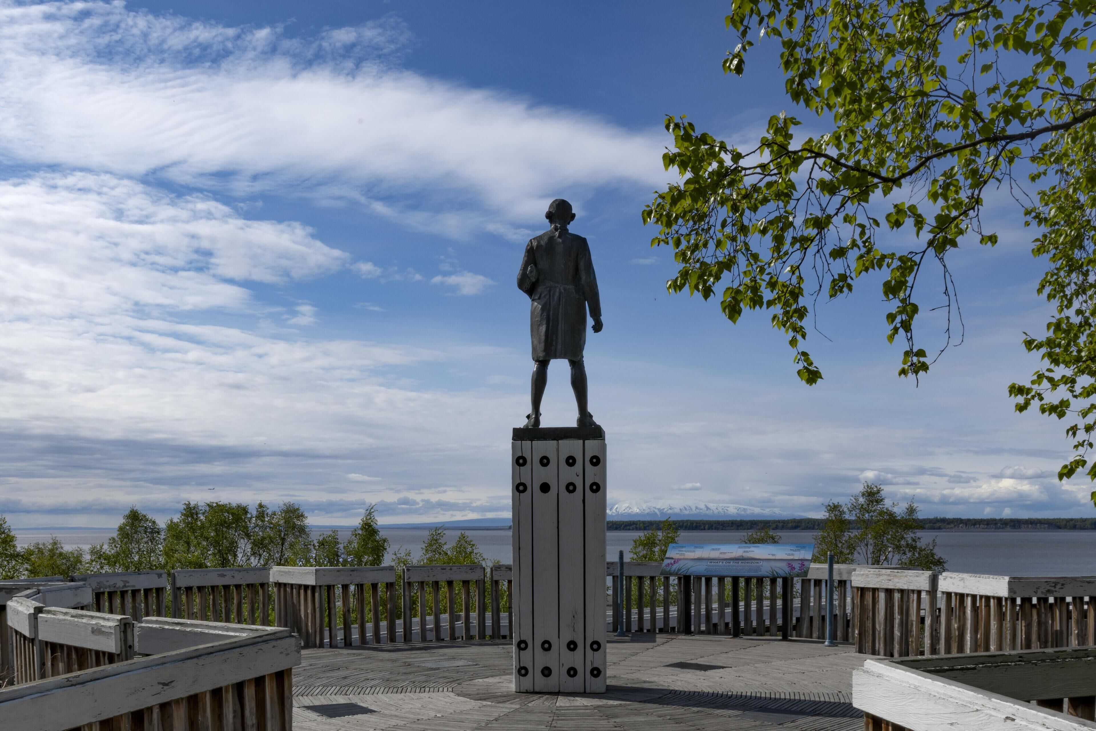 A statue on a pedestal with a view of a body of water and mountains in the background.