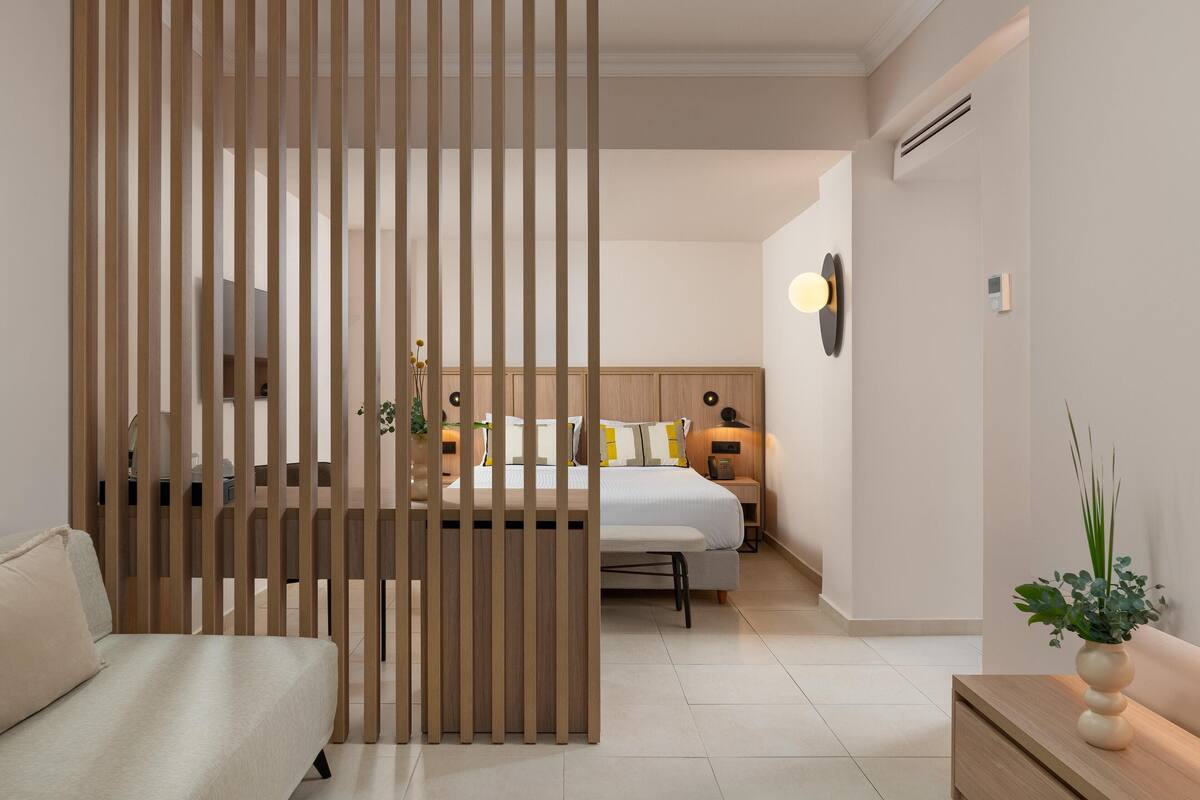 Une chambre d’hôtel moderne avec un séparateur en bois, un lit avec une literie blanche, une table de chevet avec une lampe et une petite plante en pot.