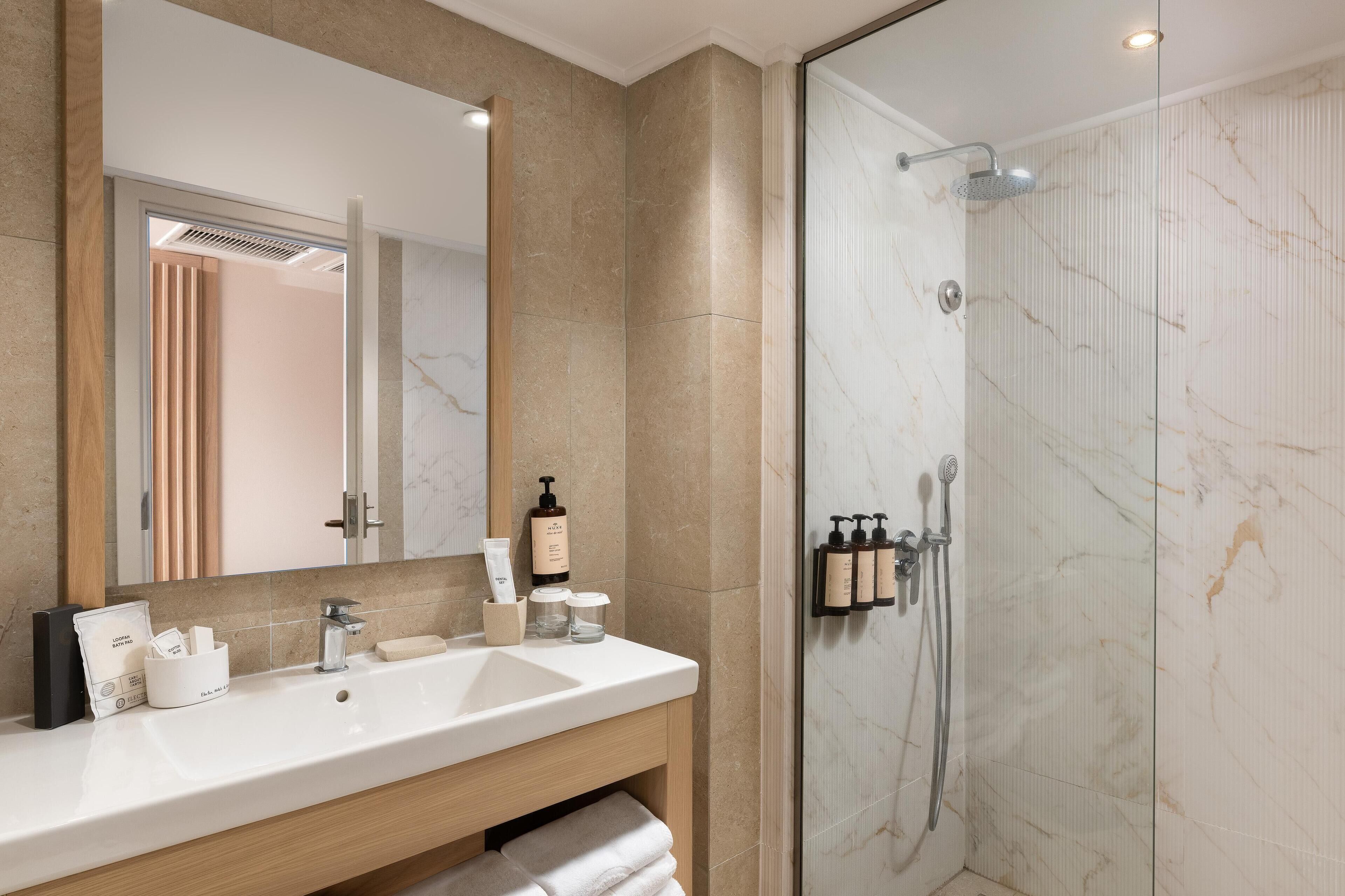 A modern bathroom with a large mirror, a white sink, and a glass-enclosed shower.