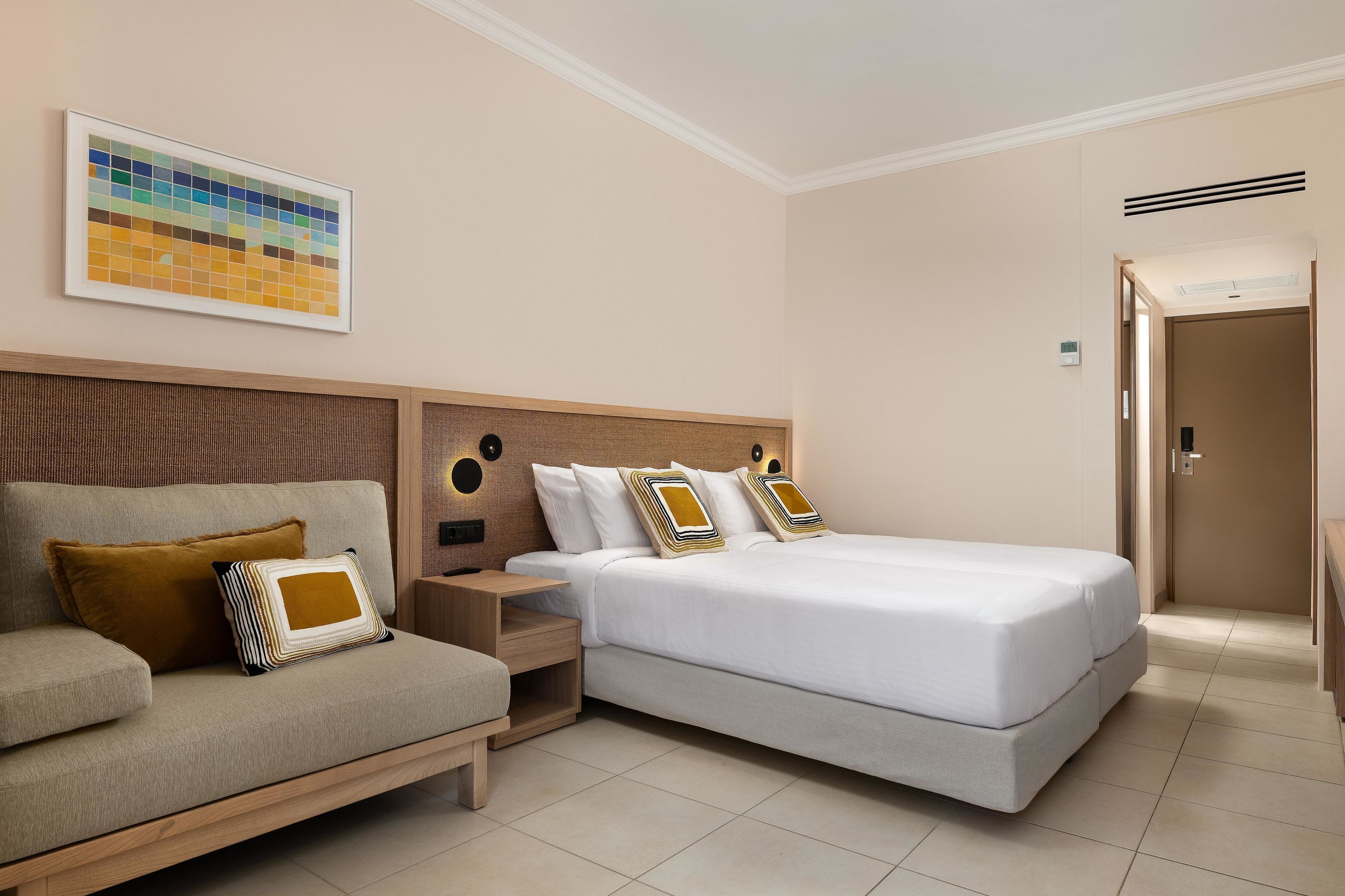 Habitación de hotel con cama, sofá, mesita de noche, una obra de arte en la pared y una puerta.