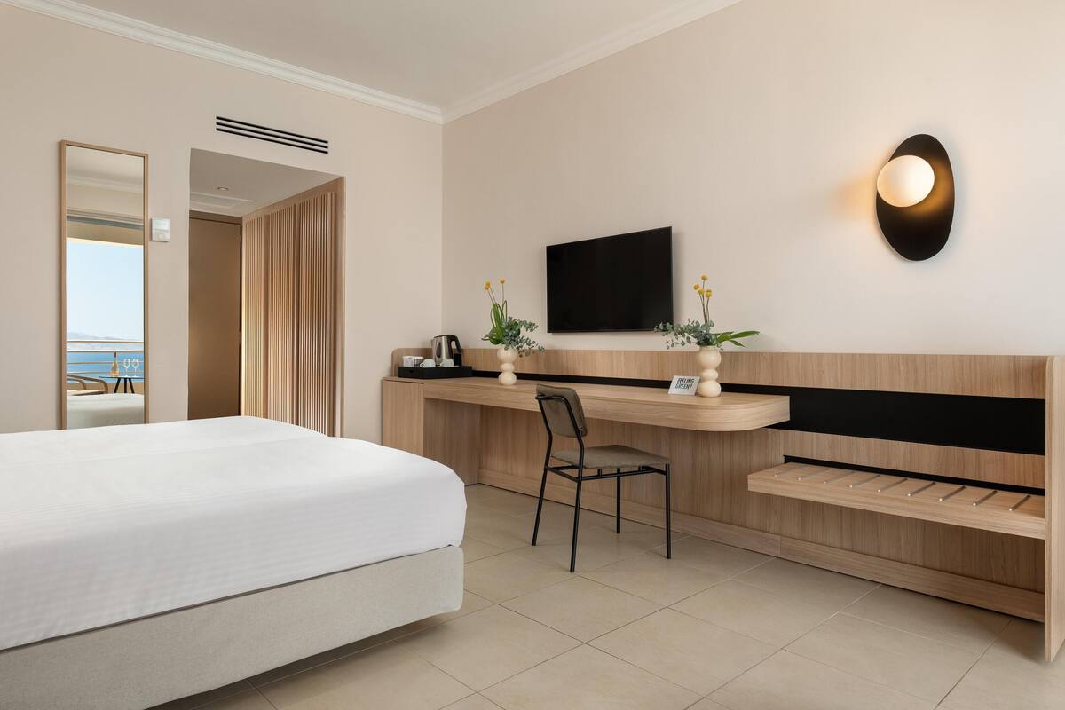 Une chambre d’hôtel moderne dotée d’un grand lit, d’un bureau avec une chaise, d’une télévision à écran plat et offrant une vue sur la mer.