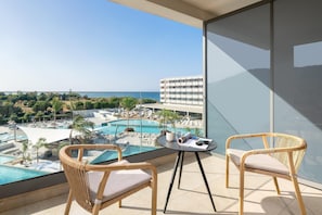 A balcony with wicker chairs, a small table, and a view of a resort pool and buildings.