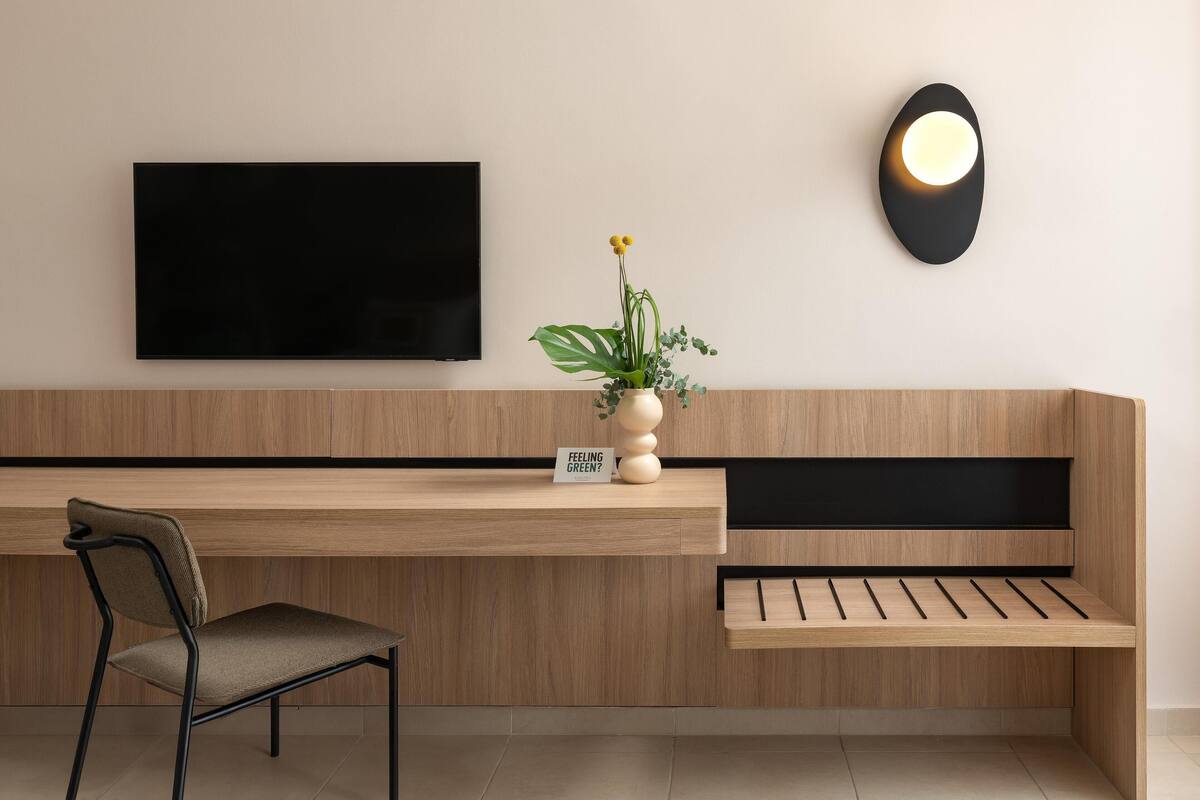 Une chambre moderne et minimaliste, dotée d’un bureau en bois, d’un téléviseur à écran plat, d’une lampe fixée au mur et d’une chaise.