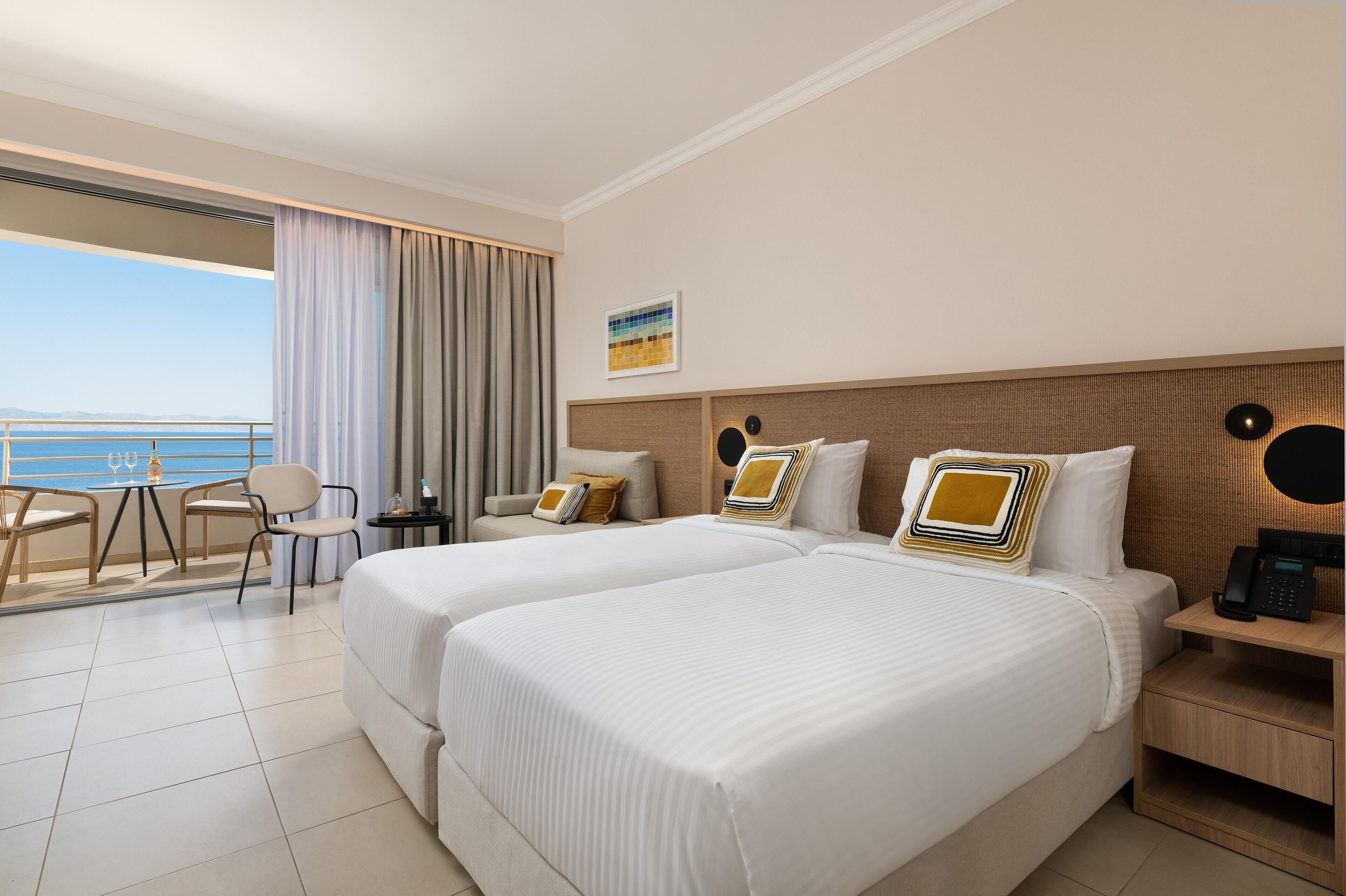 A hotel room with two beds, a balcony with a table and chairs, and a view of the sea.