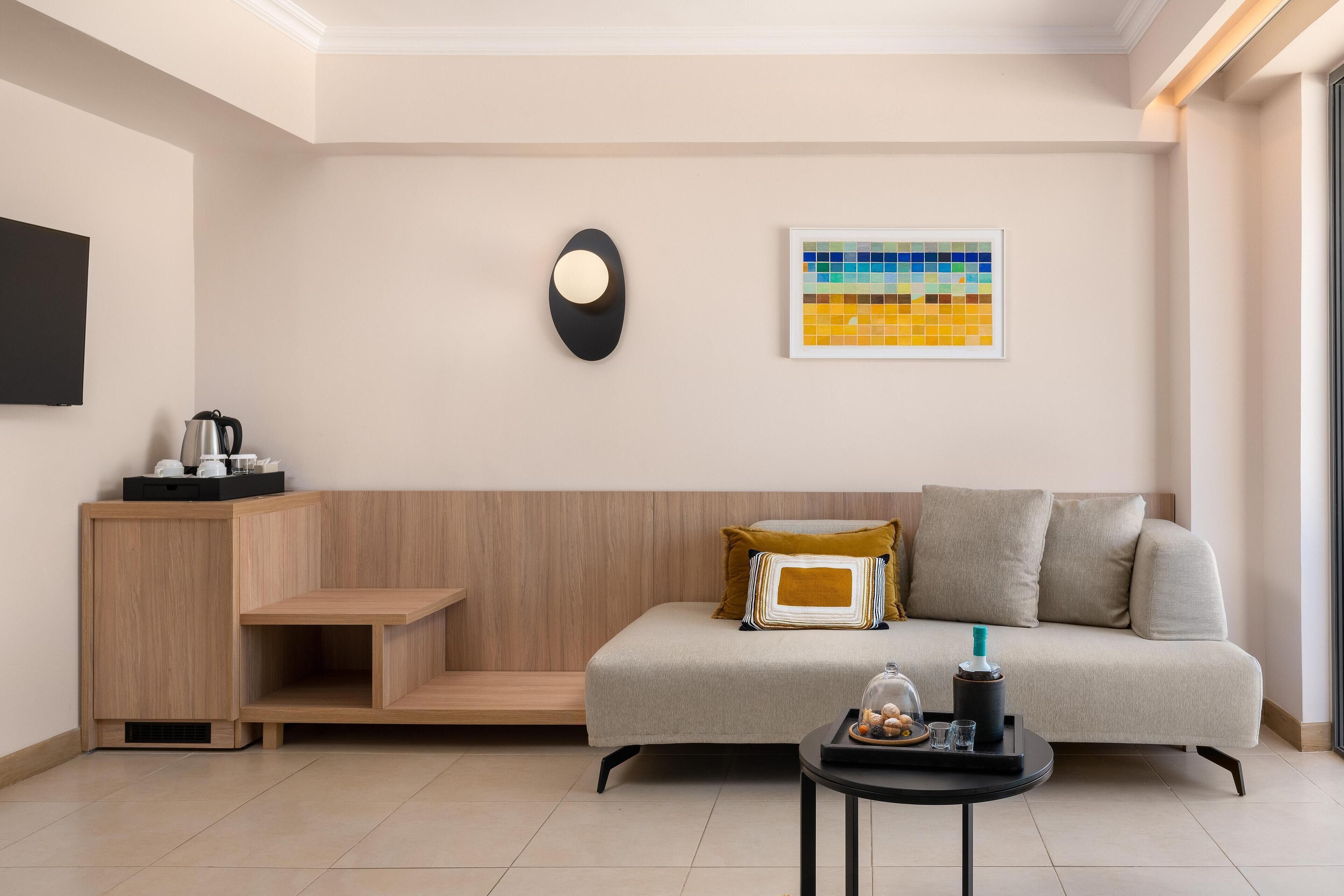 A modern living room with a sofa, a coffee table, a side table, a wall-mounted light, and a colorful artwork.