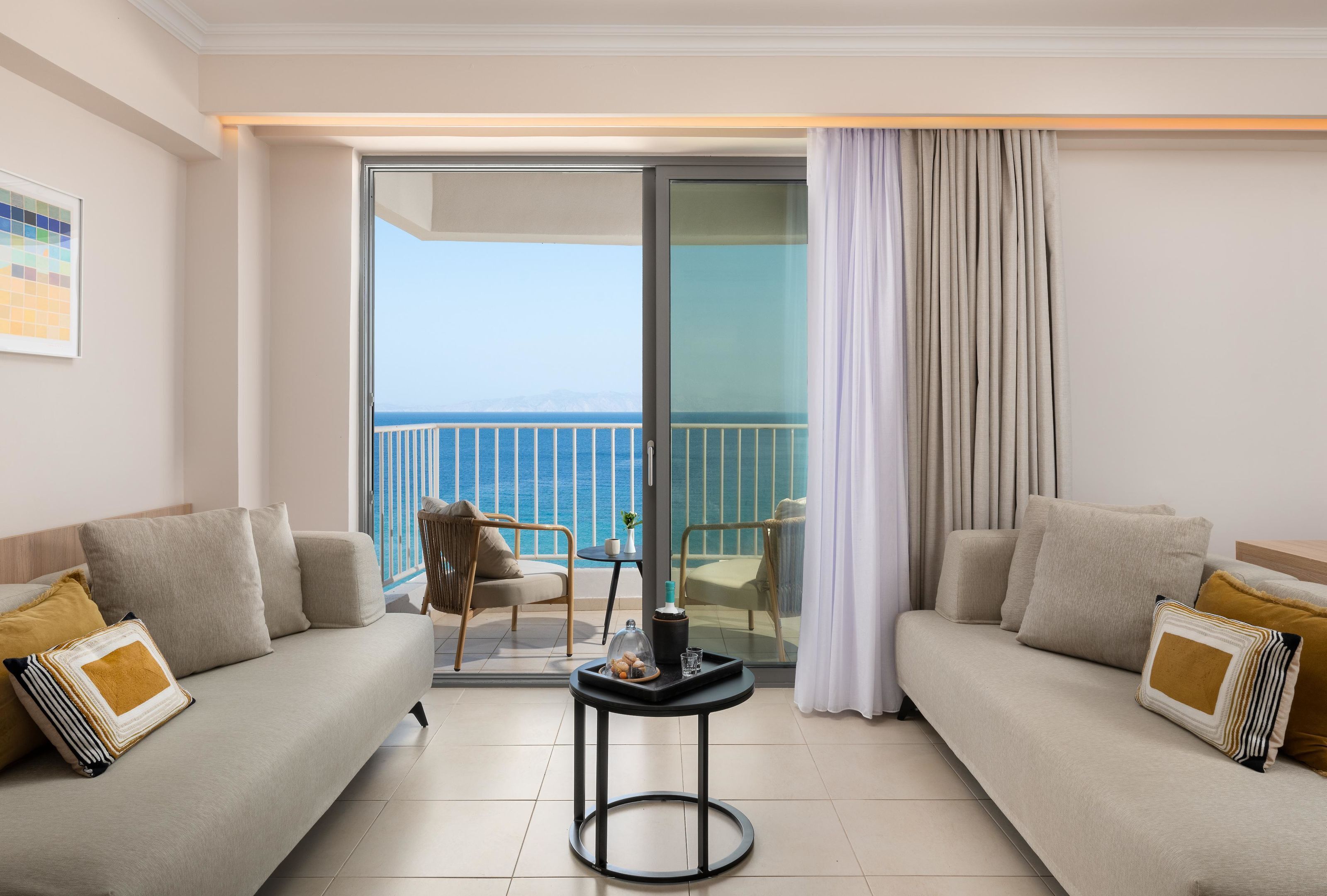Habitación de hotel con balcón, sofá, una mesita y vista al mar.