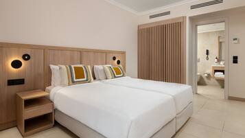 Habitación de hotel con una cama grande, una mesita de noche, un panel de control en la pared y un baño visible a través de una puerta abierta.