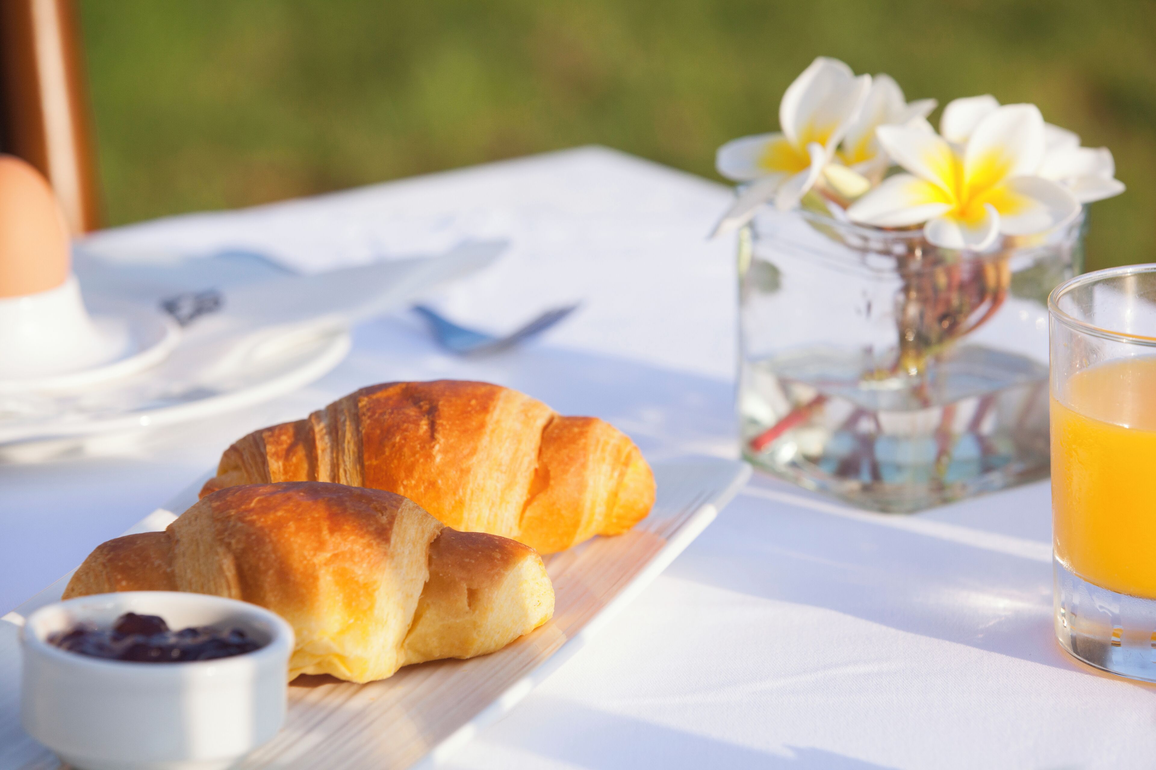 A breakfast setting with croissants, a glass of orange juice, and a small bowl of jam on a white tablecloth.