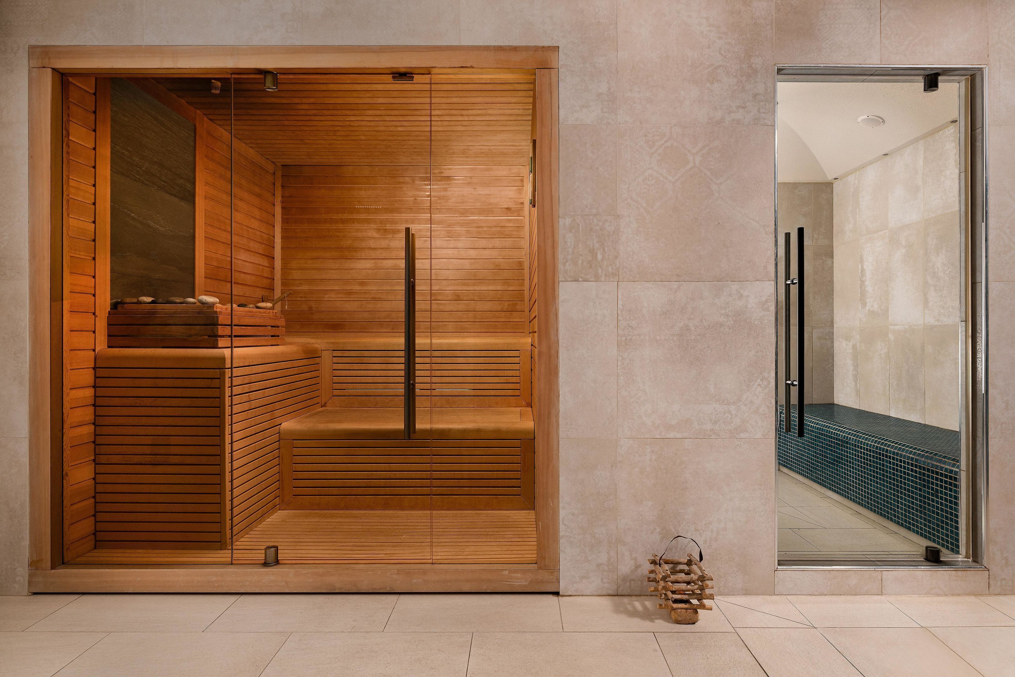 Un sauna avec des bancs en bois et une porte en verre donnant sur un espace carrelé.