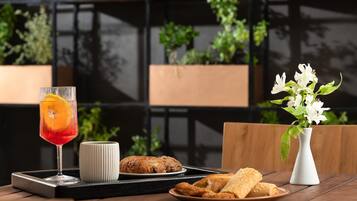 Ein Tisch mit einem Glas roter Flüssigkeit, einer weißen Tasse, einem Teller mit Croissants und einer Vase mit weißen Blumen.
