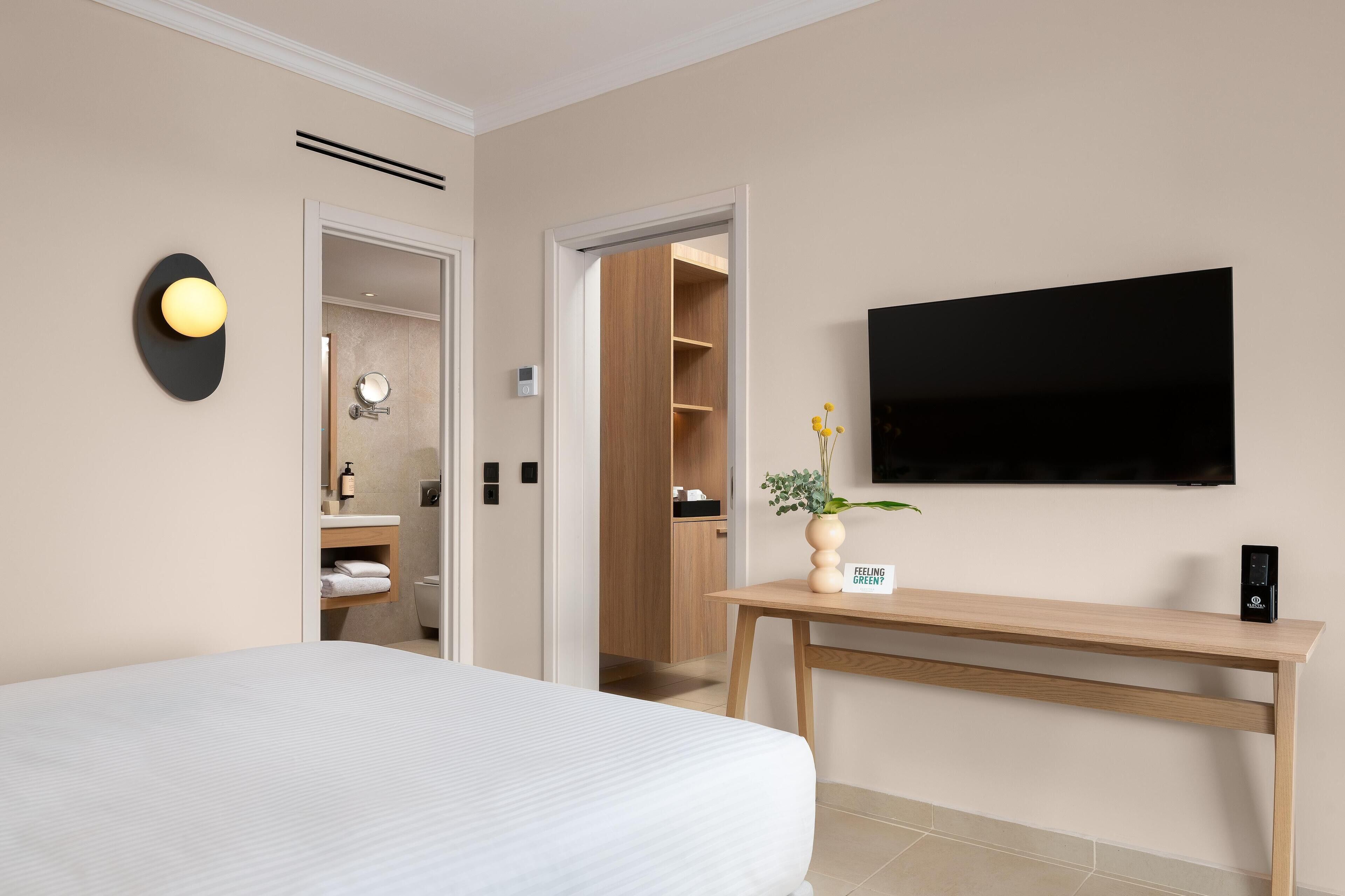 Une chambre d’hôtel comprenant un lit, une table de chevet avec une plante, un téléviseur à écran plat et une armoire en bois.