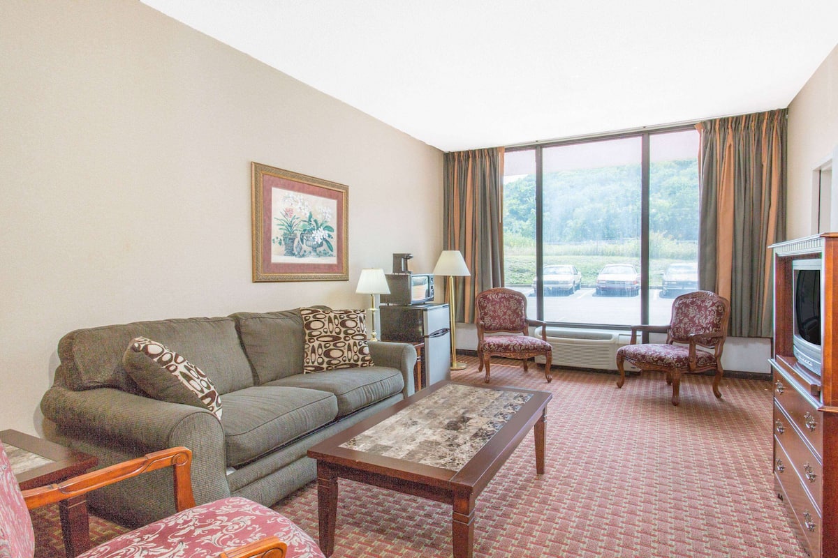 A living room with a sofa, armchairs, a coffee table, a TV, and a large window with curtains.