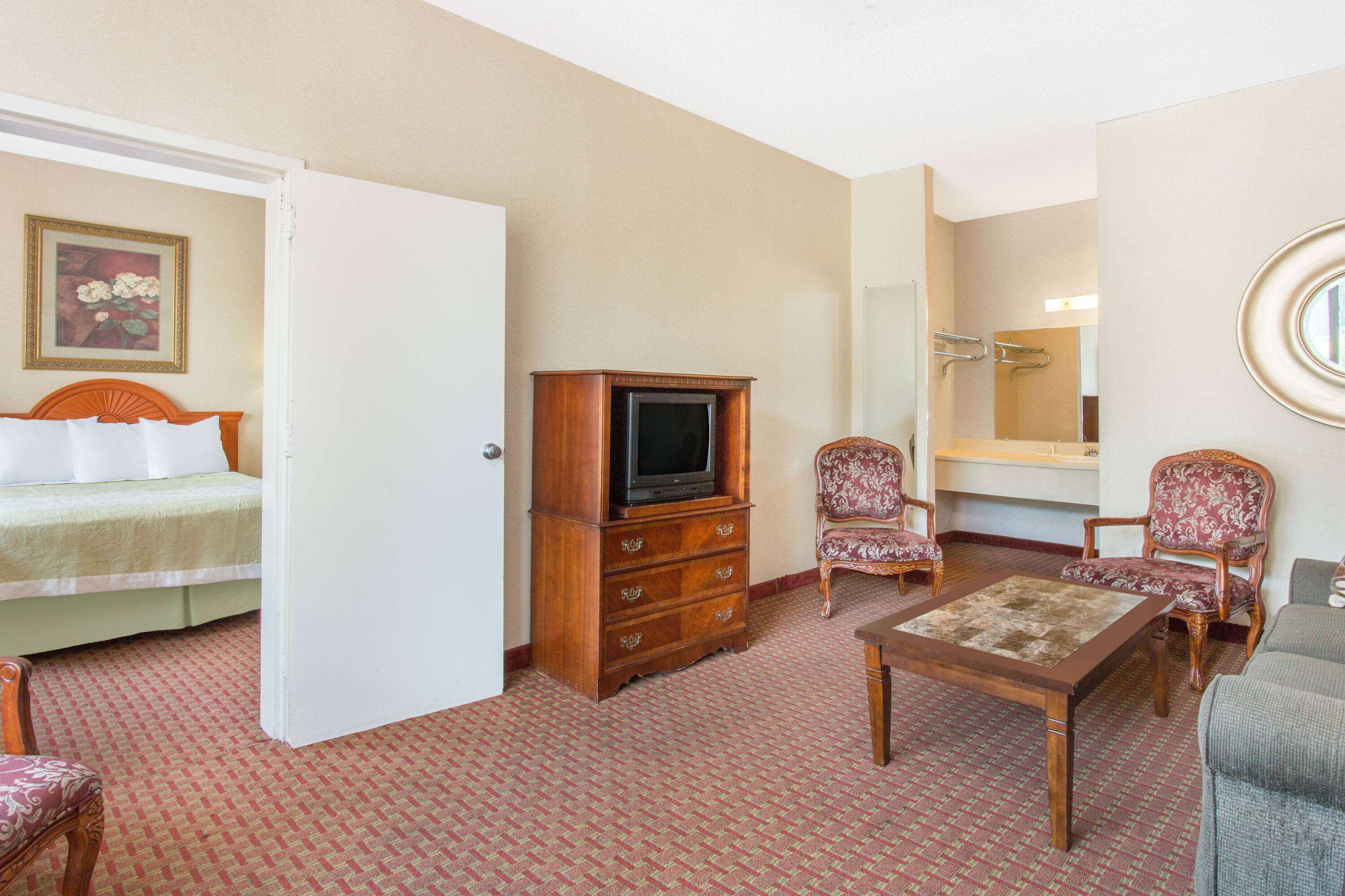 Hotelkamer met een bed, een houten dressoir, een televisie, twee gestreepe fauteuils, een bijzettafeltje en een spiegel.