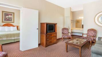 Hotelkamer met een bed, een houten dressoir, een televisie, twee gestreepe fauteuils, een bijzettafeltje en een spiegel.