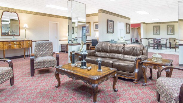 A spacious room with a large brown leather sofa, patterned armchairs, a wooden coffee table, and a red patterned carpet. - Days Inn by Wyndham Princeton (Princeton)