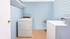 A compact laundry room with blue tiled walls, a washing machine, and a dryer. - Days Inn by Wyndham Princeton (Princeton)