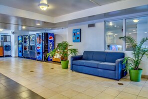 A lobby with a blue sofa, green potted plants, and a Pepsi vending machine.