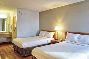 A hotel room with two beds, a bathroom with a sink and mirror, and a bedside table with a lamp and phone. - Motel 6 Buffalo, NY - Airport - Williamsville (Buffalo)