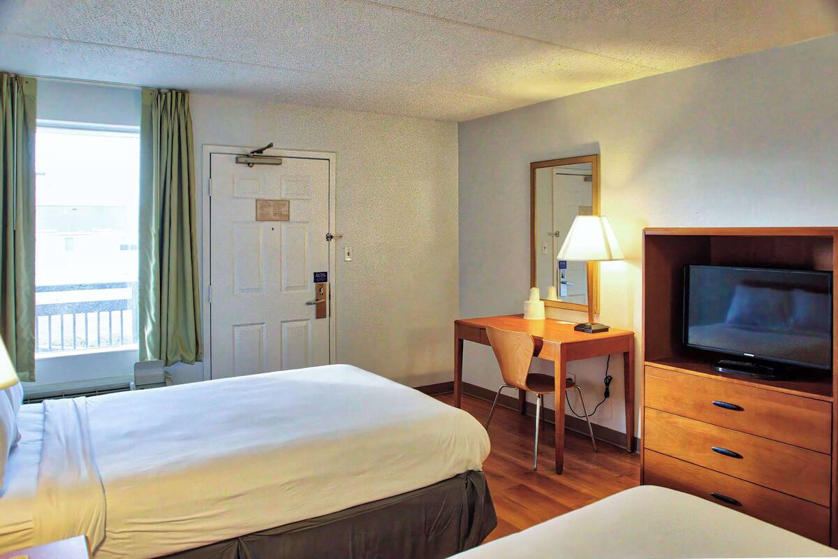 A hotel room with two beds, a desk with a chair, a television, and a window with curtains.