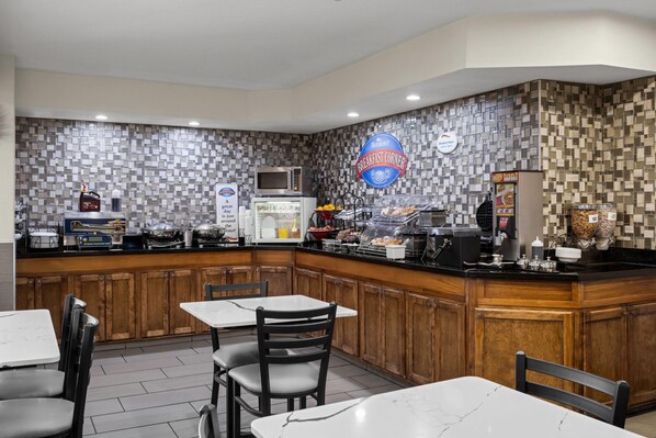 A breakfast corner with a tiled backsplash, a microwave, a coffee machine, and a variety of breakfast items on display. - Baymont by Wyndham Santa Fe (Santa Fe)