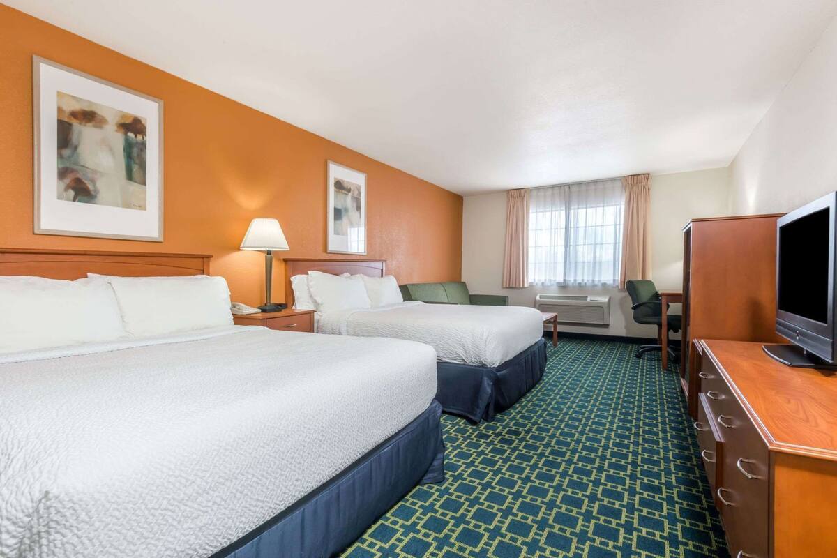 A hotel room with two beds, a desk with a television, a chair, a lamp, and artwork on the walls.