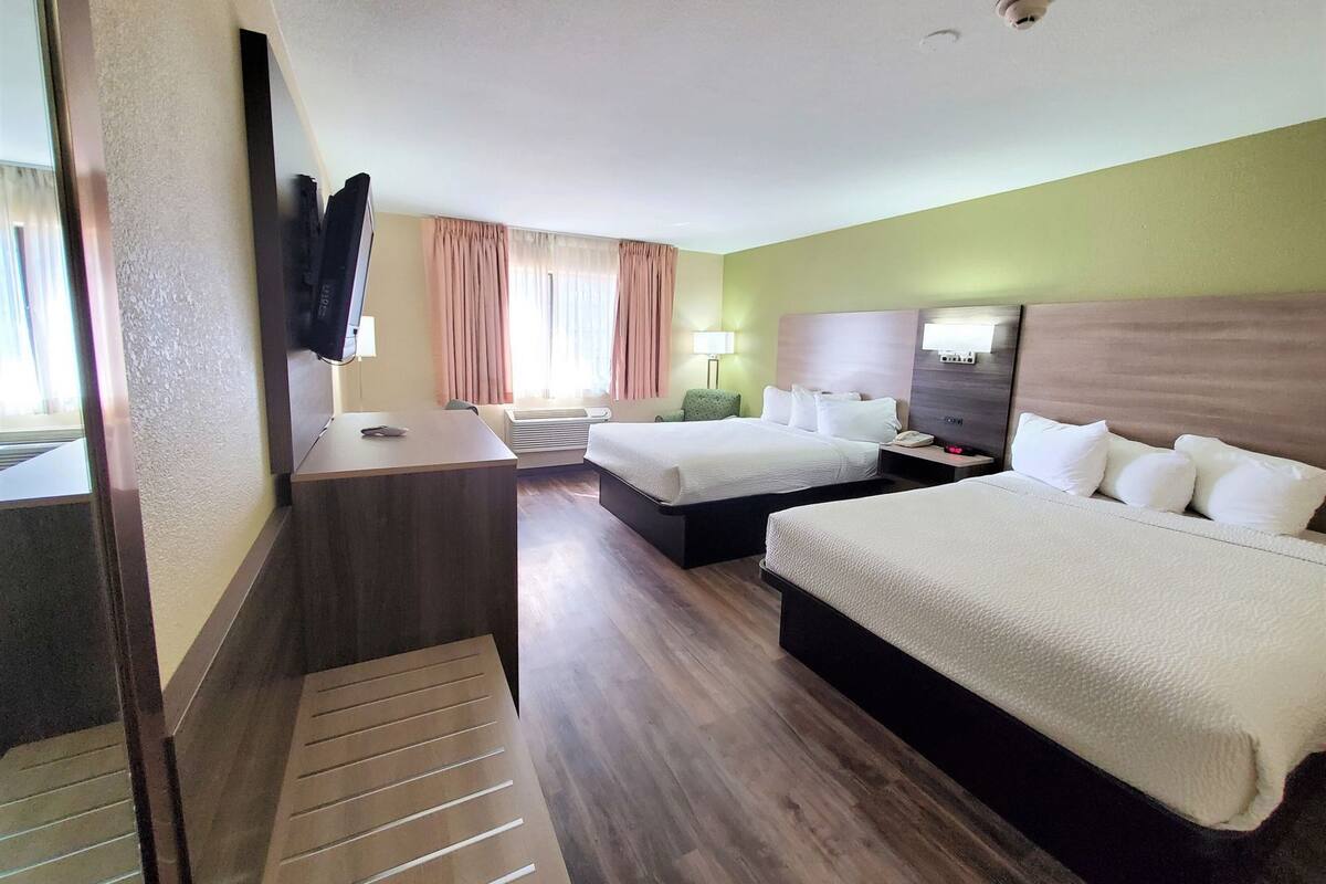 A hotel room with two beds, a desk, a TV, and a window with curtains.