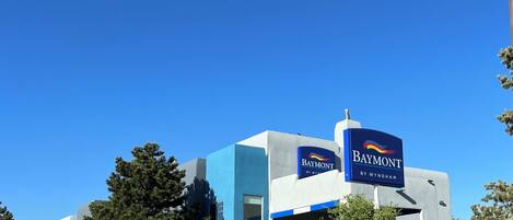 A modern hotel with a blue and white facade, a prominent 'Baymont' sign, and a parking lot with a red curb.