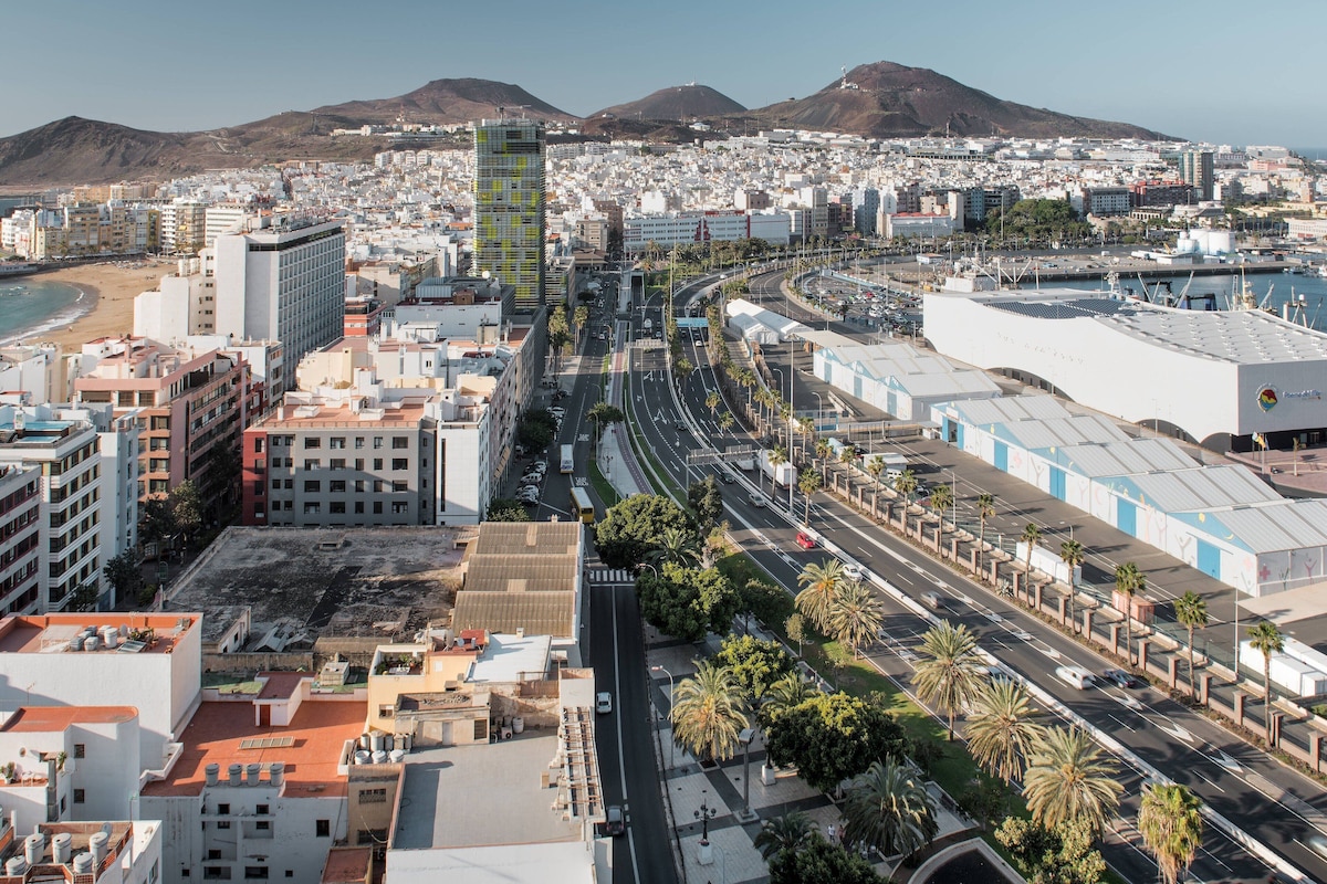 A coastal cityscape with a prominent modern building, wide roads, and palm trees.