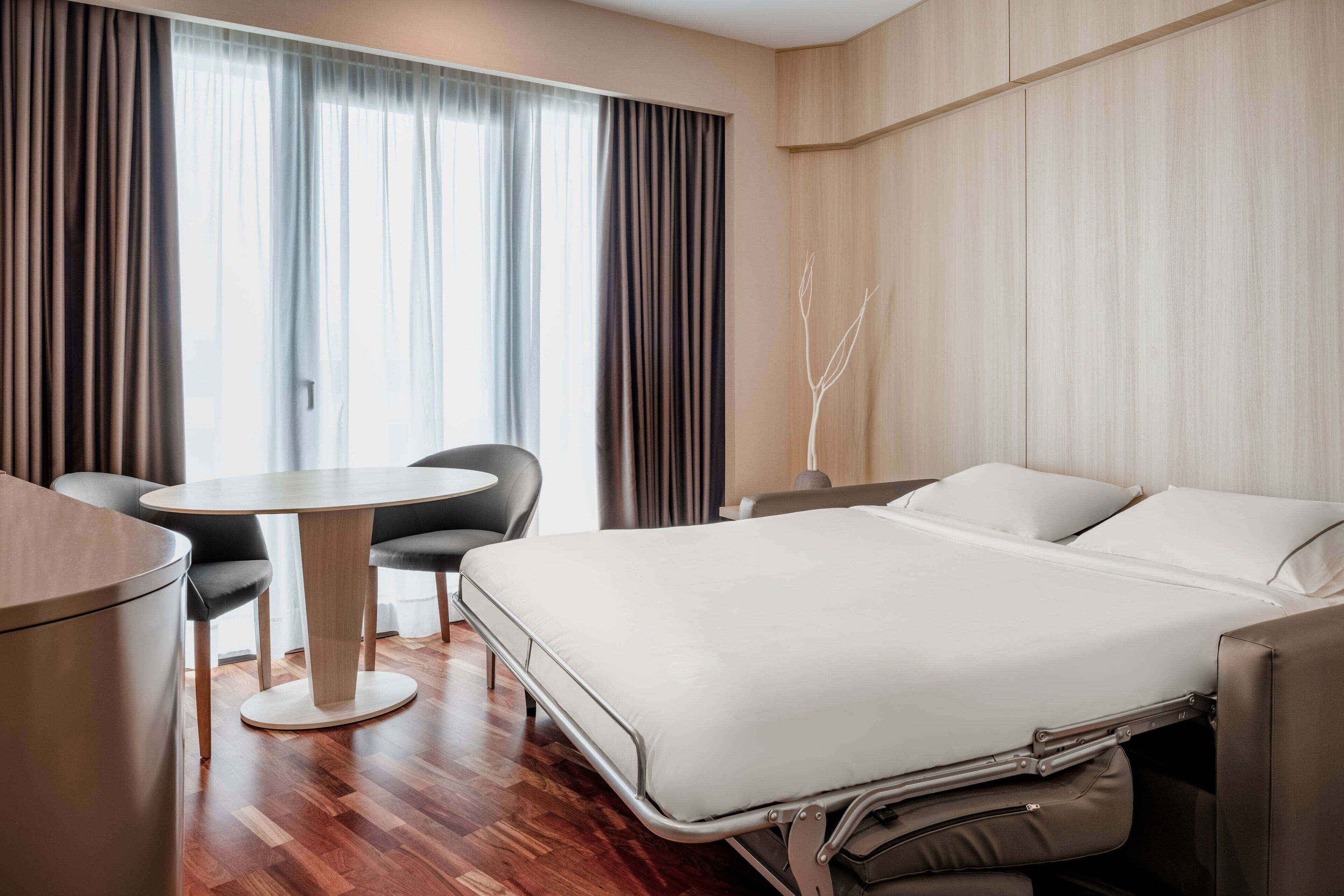 A modern hotel room with a bed, a round table, and a chair.