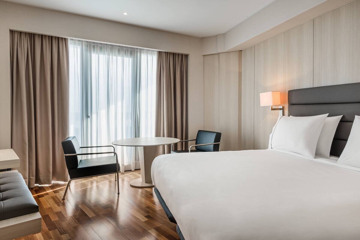 Una habitación de hotel con una cama grande, una mesa redonda, dos sillas, un escritorio y una lámpara.