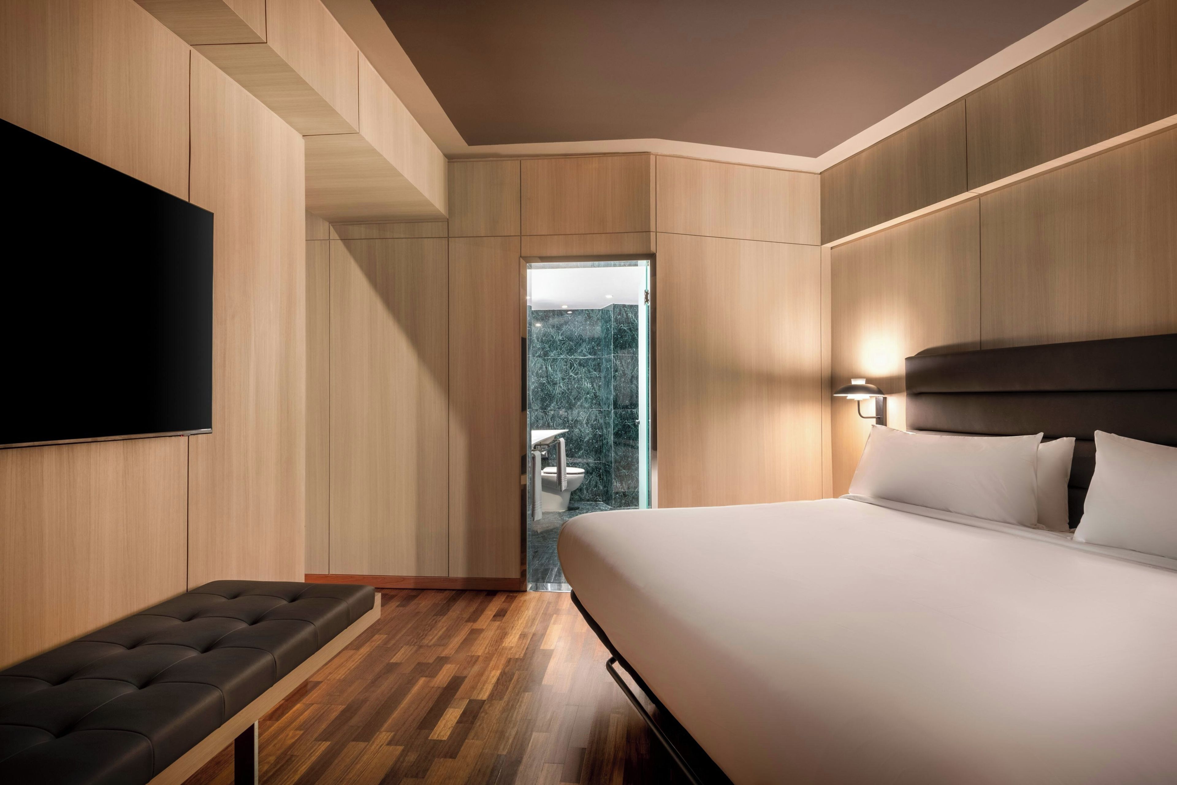 A modern hotel room with a large bed, a flat-screen TV, a seating area, and a view of a balcony.