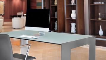 A modern office space with a glass table, a desktop computer, and a black office chair.